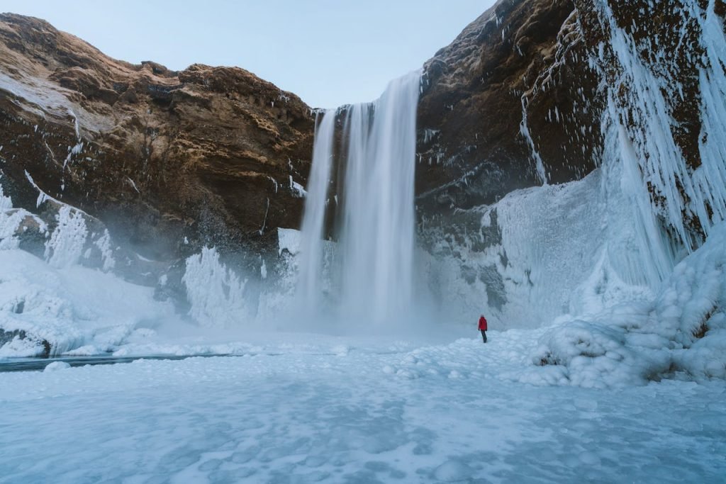 person-walking-on-snowfield-953182 A breathtaking view of a towering waterfall amidst icy landscapes in Iceland.
